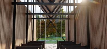 Open, wooden chapel looking through to green grass and trees.