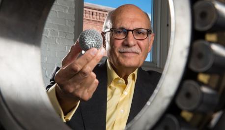 Diran Apelian looks through a large bearing while holding a small globe made with additive manufacturing