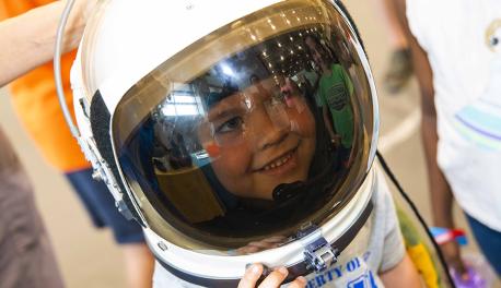 A young visitor to TouchTomorrow smiles while wearing an astronaut helmet.