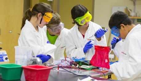 Young students compete an experiment in a lab while wearing the proper safety attire.