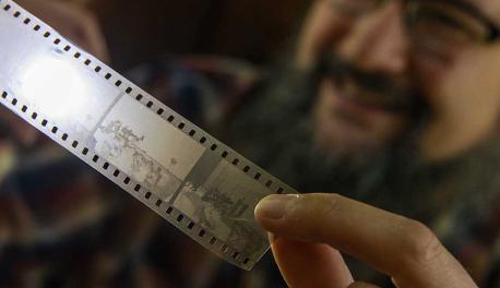 Aaron Sakulich holds a film strip up to the light while smiling in the background.