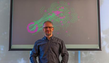 Dmitry Korkin stands before a depiction of a network of proteins that are affected by type 2 diabetes (in pink). The lines represent protein-protein interactions that are expected to affected by the mutations that are linked to types 2 diabetes.
