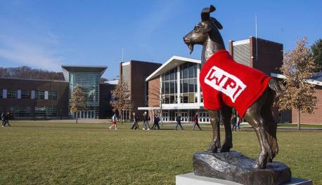 The Proud Goat statue wearing a red sweater with WPI in white letters overlooks the Quad as students walk by.