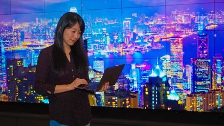 Anny Chang studies information on her laptop with a digital city landscape onscreen behind her in the Foisie Innovation Studio.