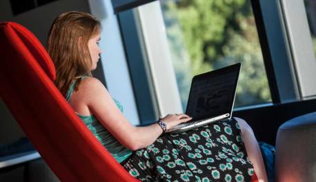 A student works on her laptop in a red chair at the Foisie Innovation Studio.