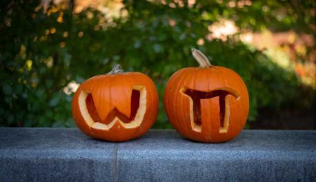 Two pumpkins sit side by side, one with a W and one with a pi symbol carved in them.