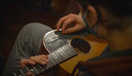 A close-up shot of a student playing guitar during an event in Higgins House.