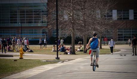 A student riding a unicycle past a busy quad