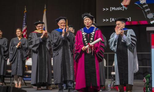 WPI President Wang stands on stage wearing the presidential medallion and holding the university charter