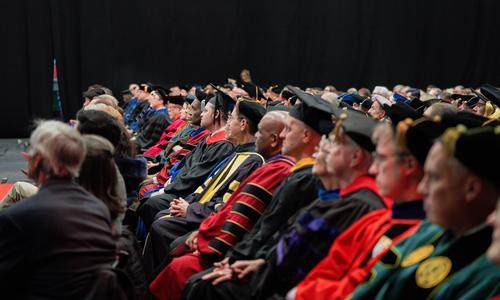 Delegates from other colleges and universities sitting at attention in the front rows and wearing their academic regalia 