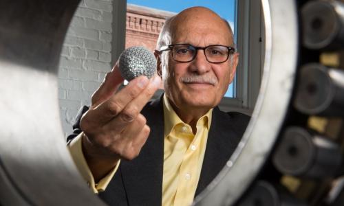 Diran Apelian looks through a large bearing while holding a small globe made with additive manufacturing alt