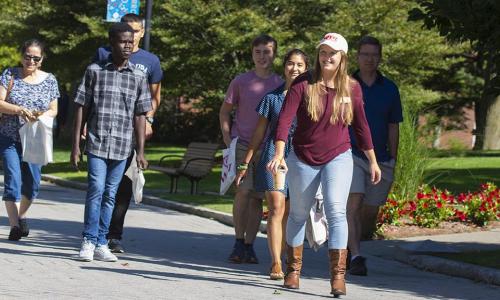 A student tour guide leads prospective students and their families along a stone path through the heart of campus.