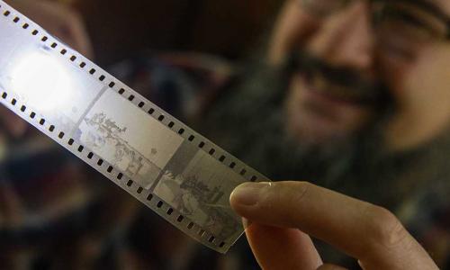 Aaron Sakulich holds a film strip up to the light while smiling in the background.