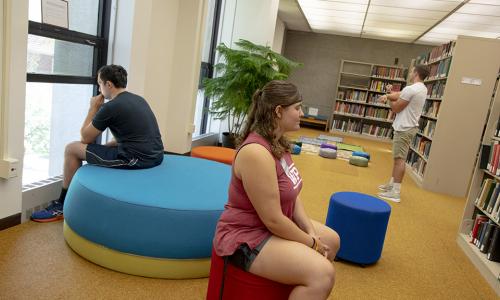 Three students engage in the library's new reflection space by stretching and meditating.