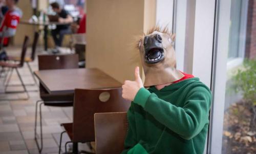 A student flashes a thumbs up while wearing a horse mask on Halloween.